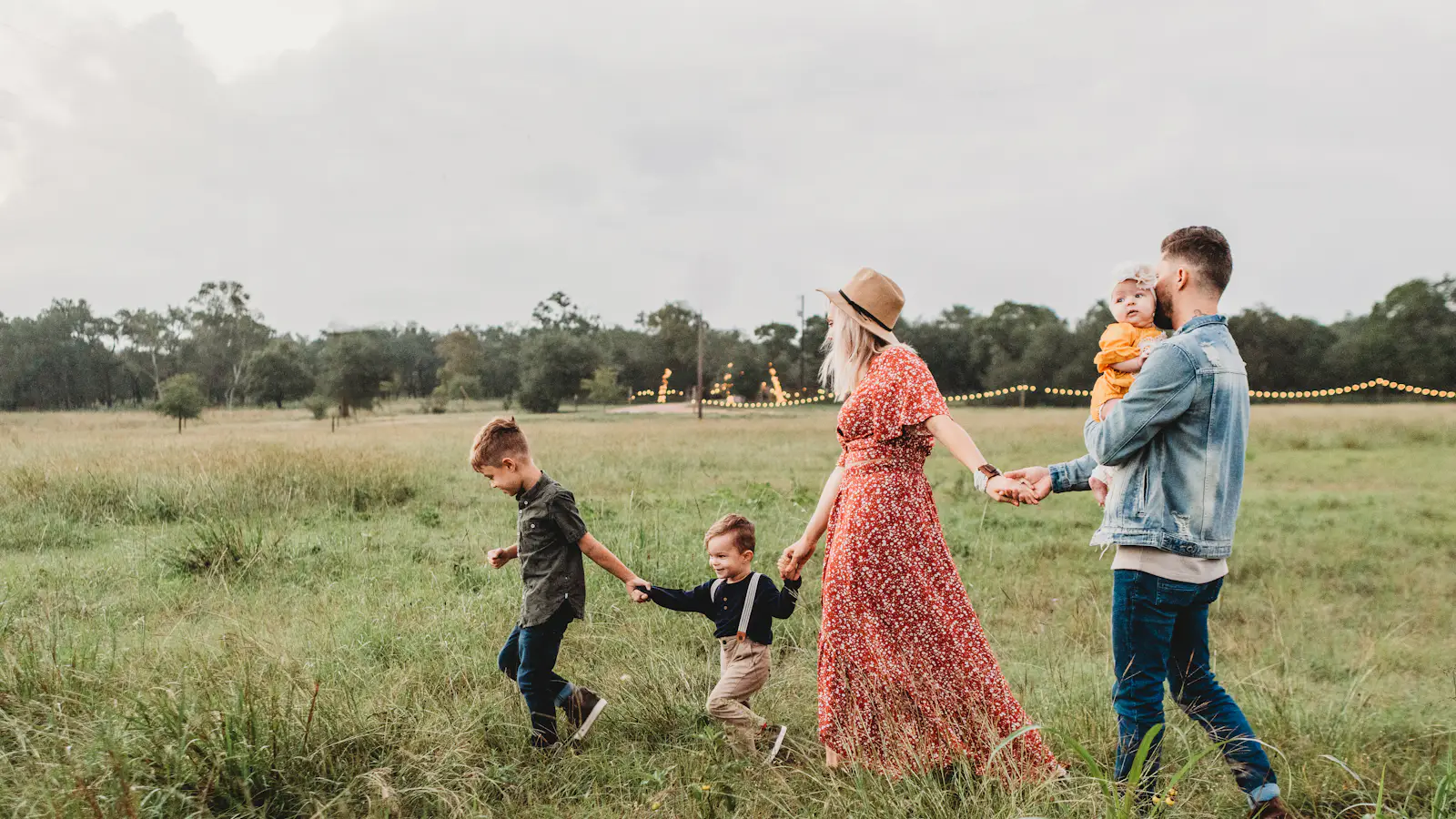 Famille avec trois enfants marchant main dans la main dans un champ