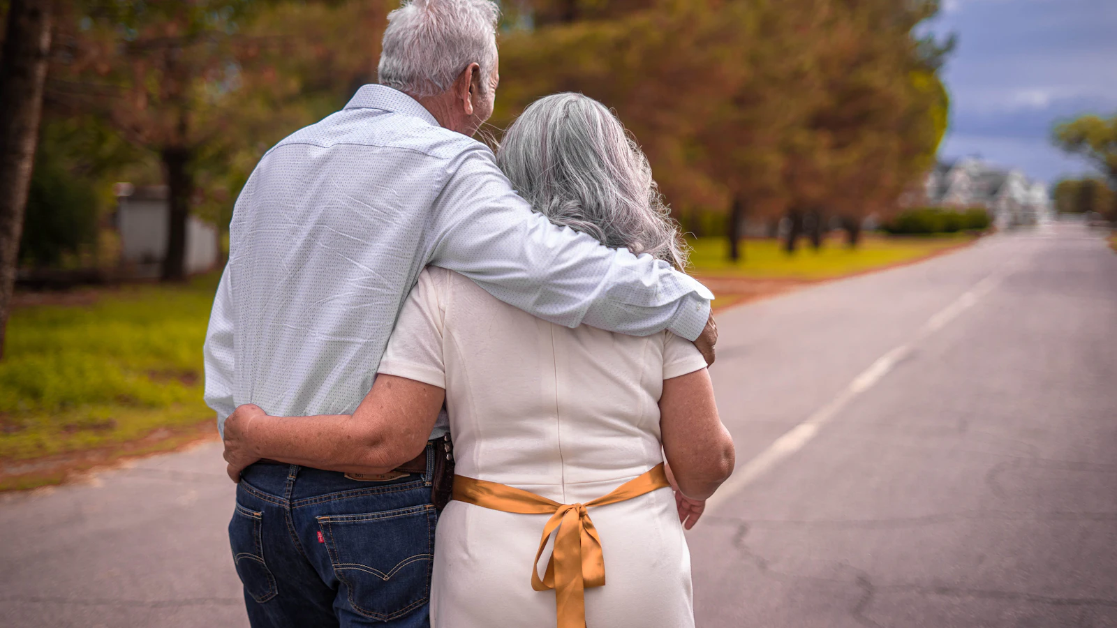 Couple de retraités marchant enlacés sur une route bordée d'arbres