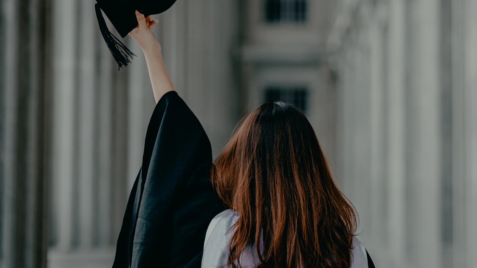 Diplômée en toge levant son mortier devant un bâtiment universitaire